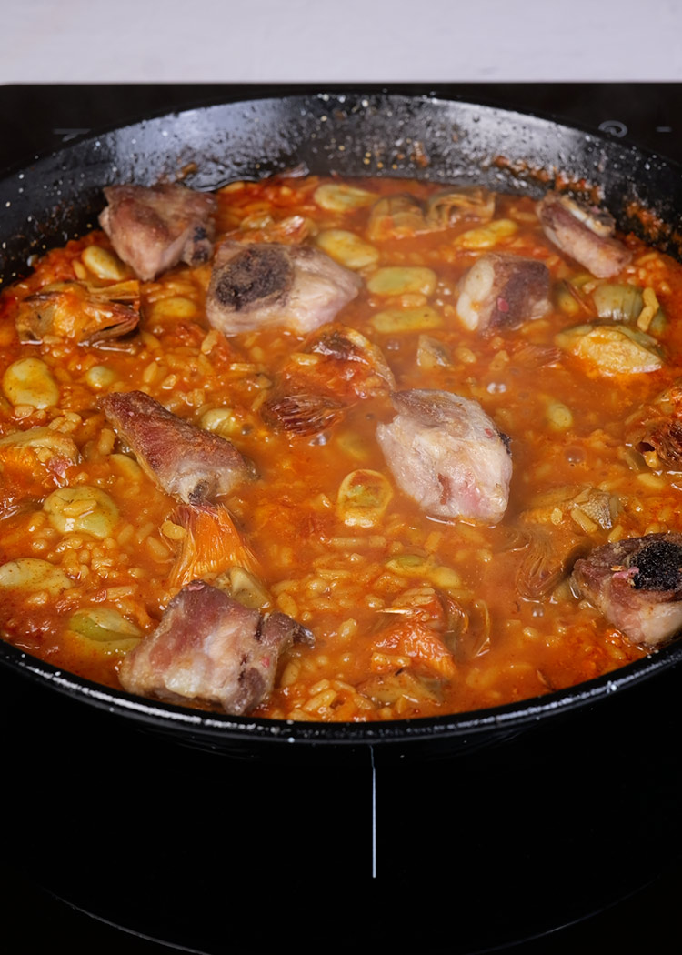 Colocar costillas en paella de habas y alcachofas